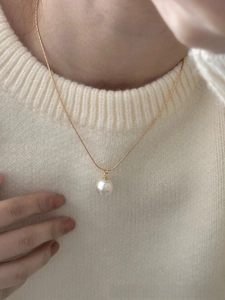 Elegant gold snake chain necklace featuring a glossy white pearl pendant on a model's neck