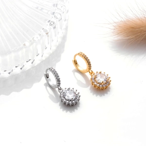 Detail of silver and gold hoop earrings with round zircon pendants on a white surface
