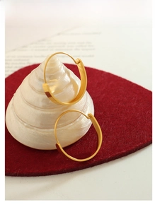 Flat golden hoop earrings on white seashell and red felt background with aesthetic book decor