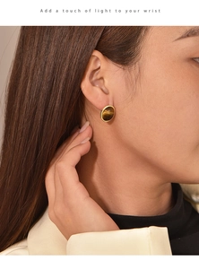 Close-up of round tiger eye stud earrings with gold plating worn by a model