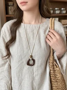 Detailed view of an ethnic resin pendant necklace paired with linen clothes and a straw bag