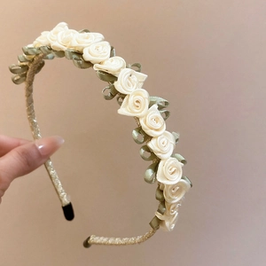 Detailed view of handmade cream fabric roses and green ribbon leaves on a woven headband