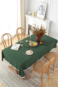 Detail of dark green cotton tablecloth with white pom-pom trim on a wooden dining table