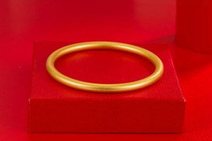 Detailed close-up of a matte gold bangle resting on a luxury red velvet jewelry box