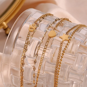 Macro view of gold-plated layering bracelets featuring heart, star, and hand charms