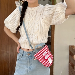 Detail of red plaid fabric crossbody bag with woven label on casual outfit