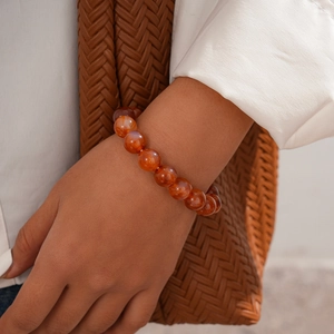Close-up of a woman wearing a red agate beaded bracelet with a warm translucent texture