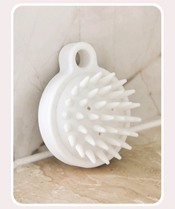 Close-up of a white silicone scalp massager brush on a marble background with a hanging hole