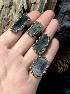 Detailed close-up of four raw green tourmaline rings with antique copper finish bands