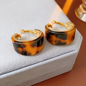 Detail of round tortoiseshell resin earrings with gold-plated clasp on a grey jewelry box