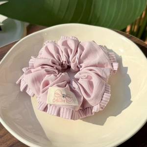 Pink striped fabric scrunchie with a logo label and rhinestone on an off-white ceramic plate