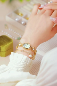 Close-up of gold quartz watch with pearl heart pendant bracelet on model wrist