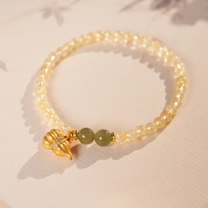 Detail von gelbem Kristall-Perlenarmband mit goldenem Anhänger und grünen Akzentsteinen