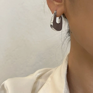 Close-up of silver chunky U-shaped hoop earring worn on ear with white silk shirt