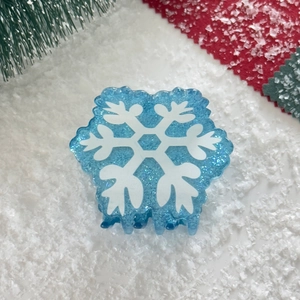 Close-up of blue snowflake hair claw clip with glitter details on festive winter background
