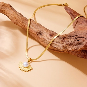 Gold fan-shaped pearl pendant necklace on flat snake chain over weathered wood