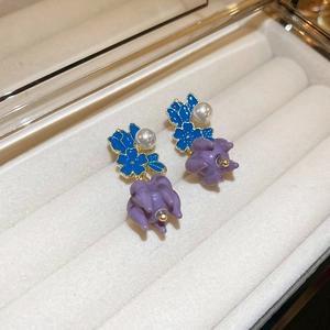 Close-up of pearl flower stud earrings with blue and purple petals in a jewelry box