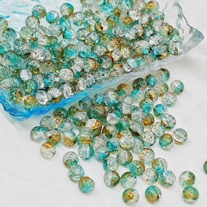 Macro detail of round teal and gold crackle glass beads on white fabric
