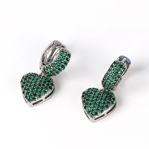 Macro detail of silver heart earrings encrusted with sparkling green gemstones