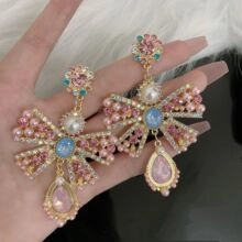 Dettaglio di orecchini da sposa a fiocco con perle rosa e pendenti in cristallo blu