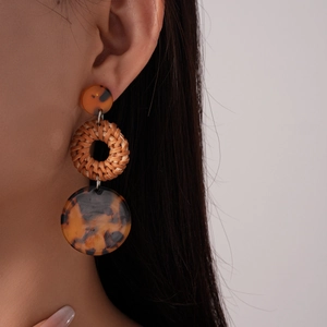 Detail of bohemian rattan and leopard resin earrings showing woven texture on a model