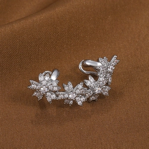 Gros plan d'un ear cuff fleur argenté serti de zircons brillants sur tissu marron