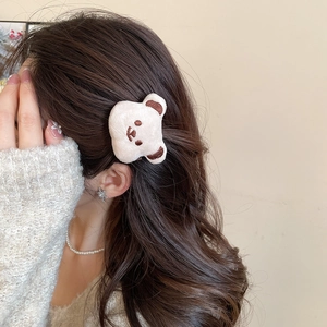 Close-up of a cute plush cream bear hair clip worn on a woman's wavy brown hair