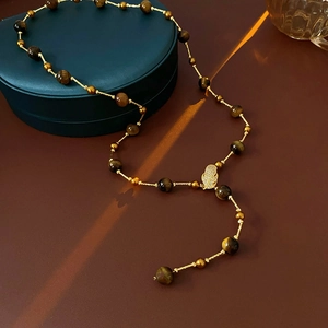 Macro shot of tiger eye beads and leaf pendant on gold zircon tassel necklace