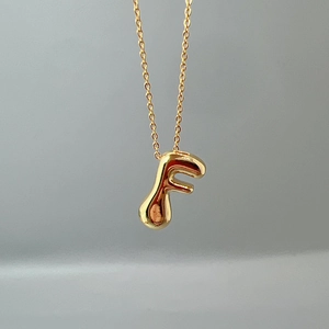Detail of a minimalist gold 3D letter F initial pendant with a polished O-link chain