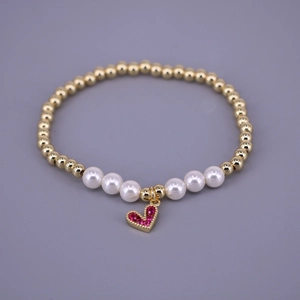 Macro detail of golden beaded bracelet with white pearls and pink zircon heart charm