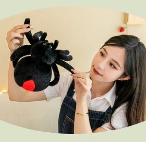 Close-up of soft black plush spider toy with red heart pattern held by hands