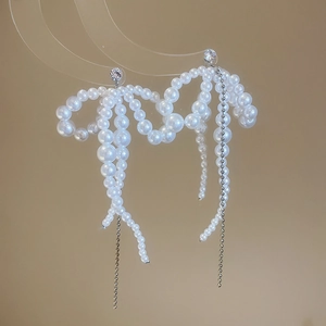 Detail view of bow-shaped pearl earrings with long tassels on a transparent stand