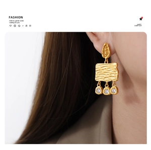 Close-up of vintage gold earrings with textured wood-grain pattern and sparkling zircons