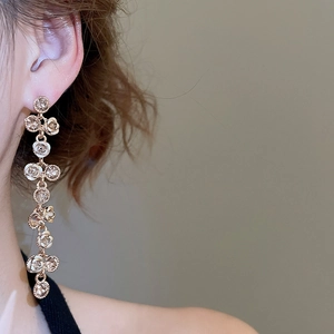 Detail of long gold drop earrings with white roses and sparkling crystals on a model