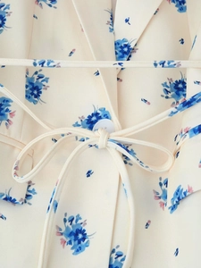 Close-up of beige floral fabric with blue prints, waist tie knot, and button detail