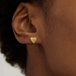 Detail of a golden heart stud earring with micro white crystals on a model ear