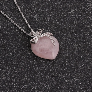 Close-up of pink quartz heart pendant with silver bow decoration and twisted chain