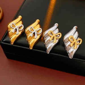Close-up of diamond-shaped bow earrings in gold and silver finish on black leather