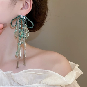 Long tassel earrings featuring green bow and leaf charms worn by a model in a side view
