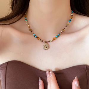 Close-up of beaded necklace with gold sun pendant and turquoise stones on neck