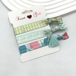 Detail of three knotted elastic hair ties with palm tree charm and tassel accents