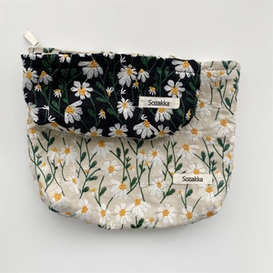 Detailed embroidery of white daisies on beige and black textile cosmetic storage bags