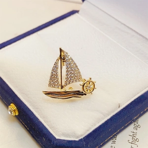 Detailed macro view of a golden sailboat brooch with sparkling zircons in a blue velvet box