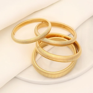 Set of four gold-colored elastic spiral bracelets with ribbed texture on white silk