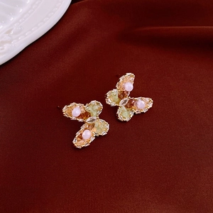 Macro detail of gold butterfly stud earrings with pink and green crystals on red velvet