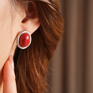 Close-up of a model wearing a large red oval gemstone earring with silver matte base