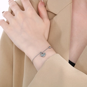 Detail of silver heart bracelet with dark shell inlay worn on wrist with beige blazer