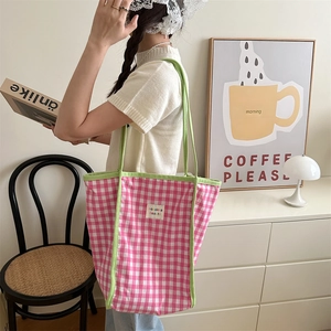 Pink and white checkered canvas tote bag with green handles shown in a lifestyle indoor setting