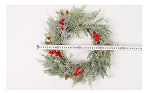 Measuring the diameter of a green Christmas wreath with red berries and small pine cones