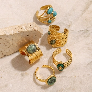 Détail de bagues bohèmes dorées avec pierres naturelles turquoise et vertes sur marbre